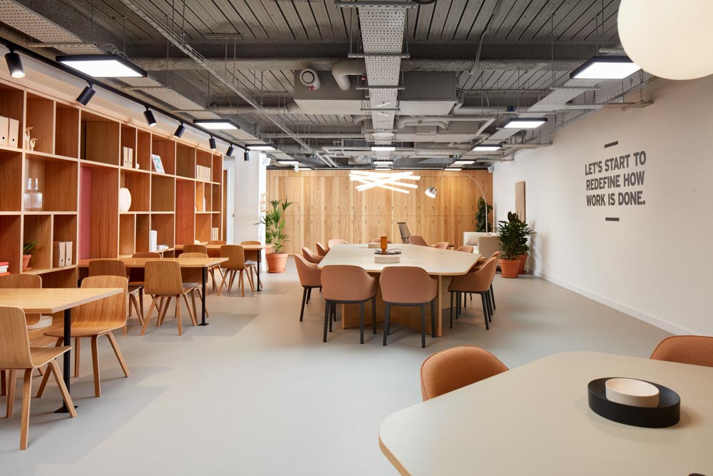 FT Architects - New Broadhouse - Project Image 2 Open co-working space with oak shelving, terracotta chairs and a 'redefine how work is done' wall graphic.