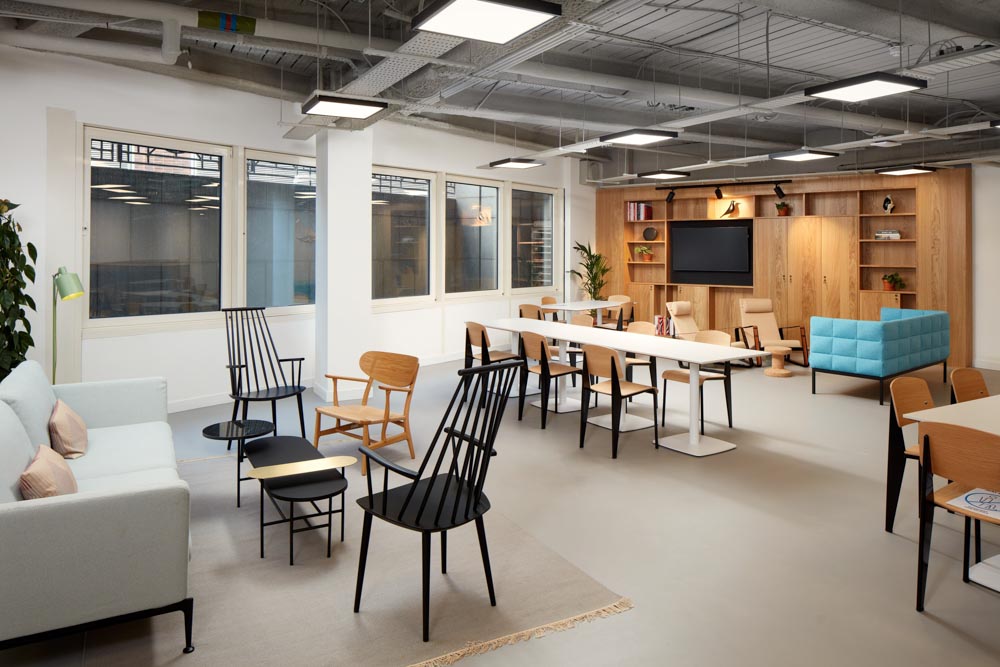 FT Architects - New Broadhouse - Project Image 6 Breakout lounge with black spindle chairs, a blue tufted sofa and a timber media unit by tall windows.