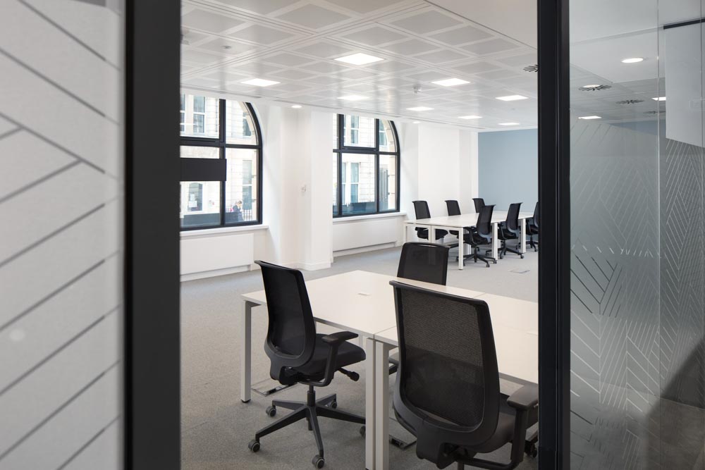 FT Architects - New Broadhouse - Project Image 7 Private serviced office seen through a patterned glass partition, with arched windows and white desks.