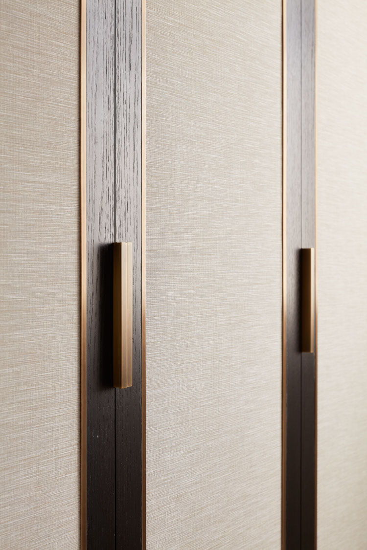 ft-architects-ovington-square-joinery-detail Close-up of bespoke wardrobe doors in grasscloth and dark timber with bronze handles
